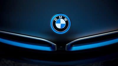 Frontaufnahme des leuchtenden BMW-Logos in Blau und Silber auf dunklem Fahrzeugkleid, mittig angeordnet über einer markentypischen Niere.